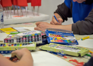 2 Menschen malen mit Buntstiften kreativ auf Papier und sind konzentriert.